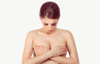 A woman considering breast cosmetic surgery holding with hands and looking down at her breasts